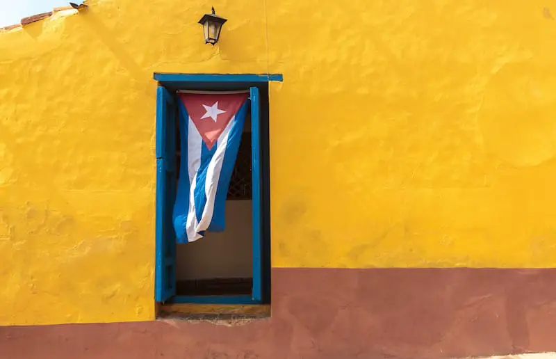 cuban flag handing from window in brightly painted yellow house