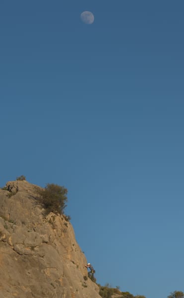 rock climber on the top of a climb with moon seen in the background