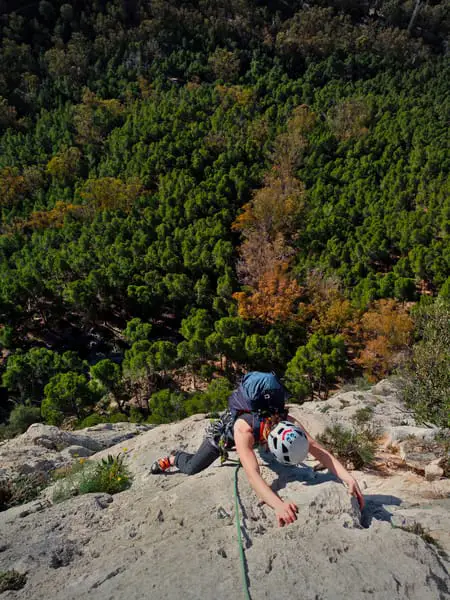 woman mult-pitch rock climbing in span with green trees in background