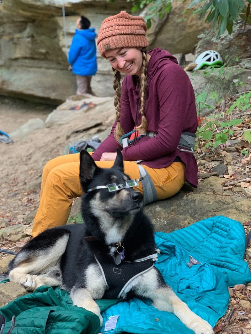cute dog wearing belay goggles sitting with rock climber
