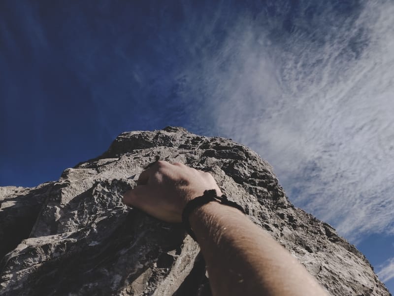 man with watching grabbing rock while climbing