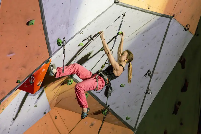 Women climbing advanced overhung route with red-orange pants