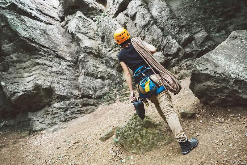 Young woman with climbing equipment goes to a rock outdoor, rear view