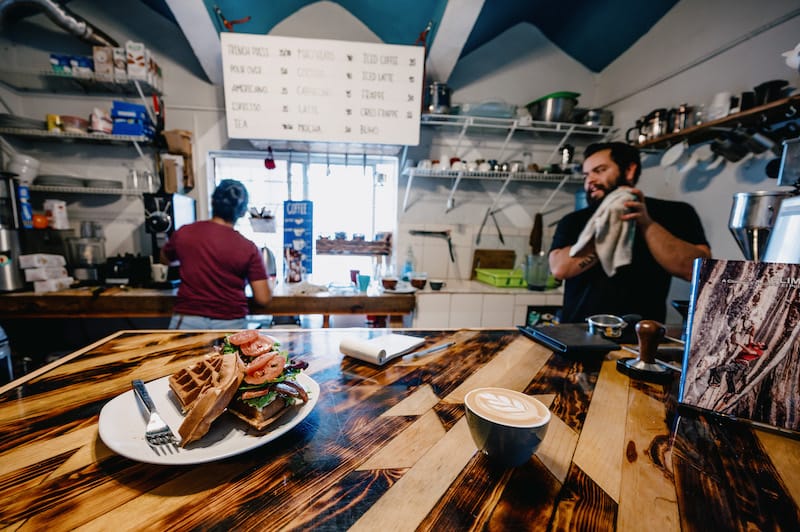 Two workers preparing food at el buho with food and coffee on the counter