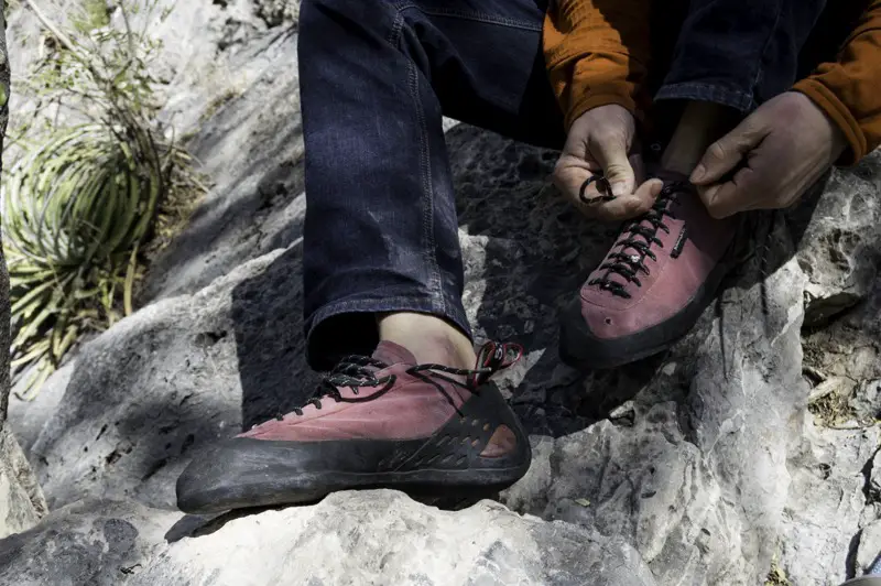 Male rock climbing putting on pink lace up climbing shoes
