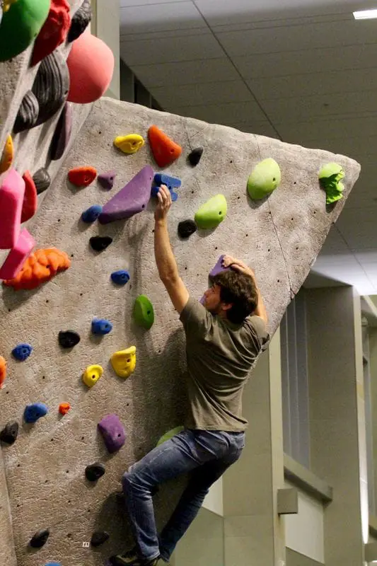 Man bouldering in gym reaching for purple sloper