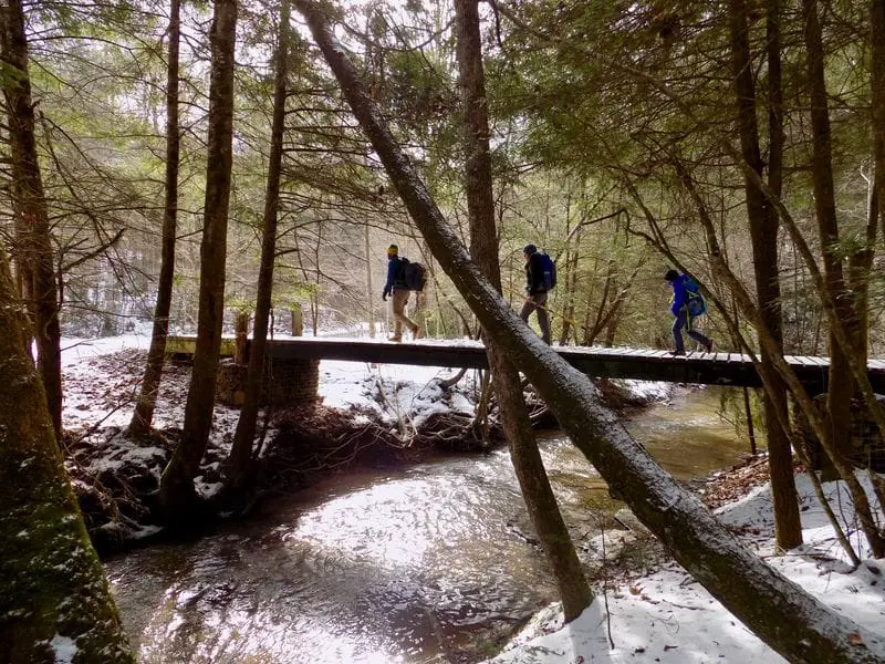 Three climbers crossing wood bridge with snowy background in daniel boone forest
