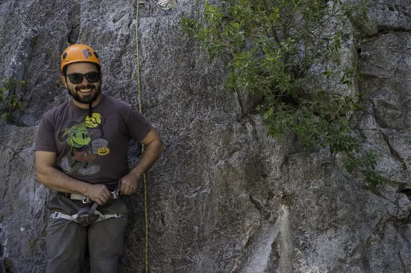 Climber with orange helmet smiling while adjusting his harness 
