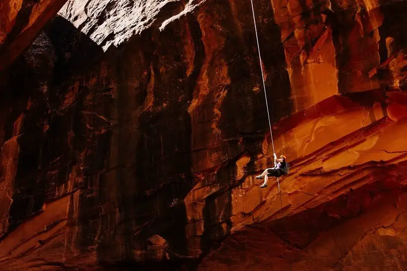 Man doing hanging rappel over cave with red sandstone